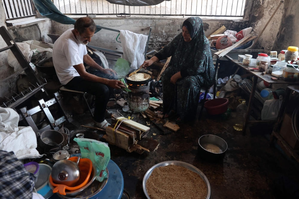 Displaced Palestinian Nazek Abu Shmala roasts stale bread crumbs to make a traditional sweet pie (knefeh) for her family, as her husband Saber looks on, inside a flat in the Jabalia refugee camp in the northern Gaza Strip where she's temporarily sheltering with her family on August 15, 2024,amid the conflict between Israel and Hamas. — AFP pic