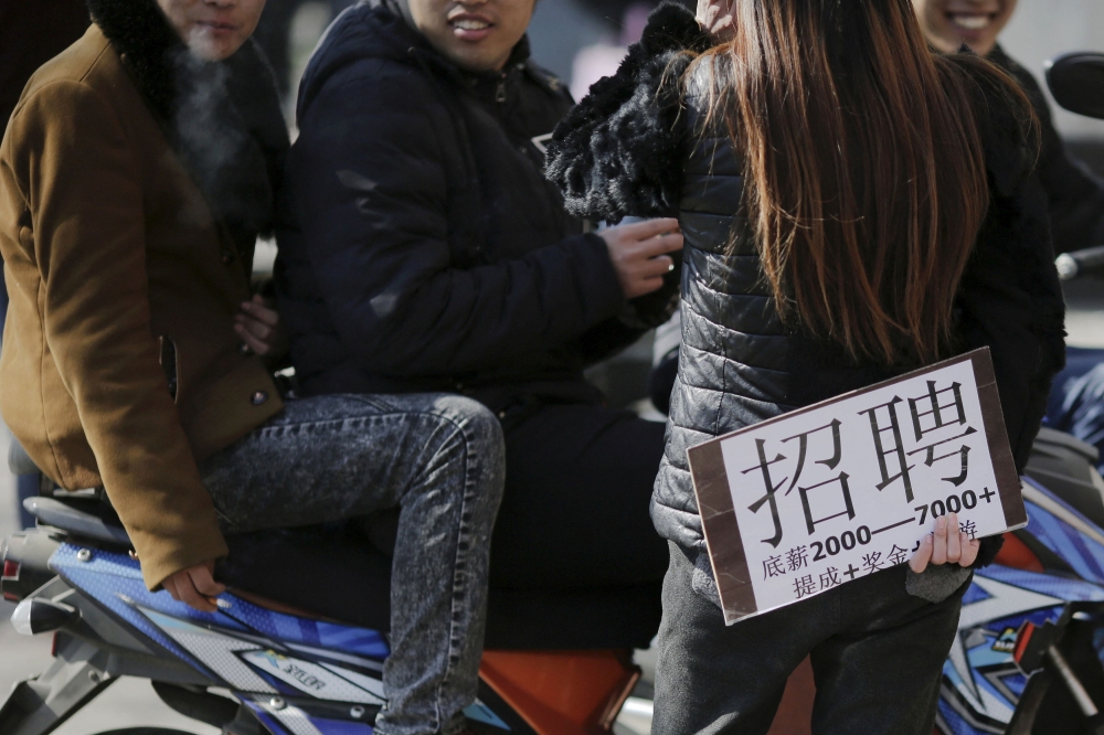 A recruiter holding a placard advertising jobs talks to young men at an unofficial job market in suburbs of Beijing February 24, 2016. — Reuters pic  