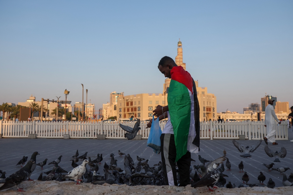 A man wearing a Palestinian flag feeds the birds near the Fanar Mosque with its spiral minaret in the Qatari capital Doha August 16, 2024. Gaza ceasefire talks in Doha paused yesterday with negotiators to meet again next week seeking an agreement to end fighting between Israel and Hamas and free remaining hostages. — AFP pic