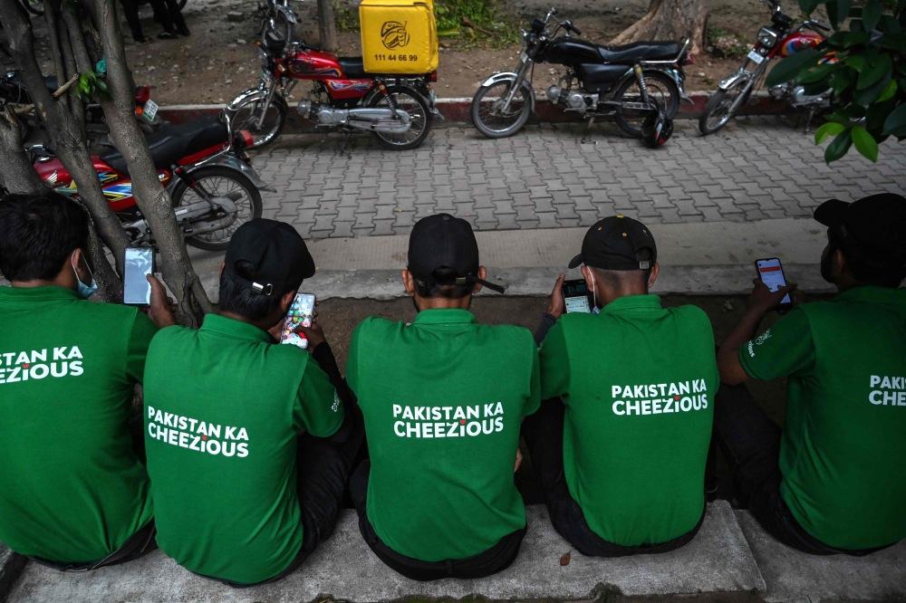 Food delivery men use their mobile phones as they sit near a restaurant in Islamabad on August 17, 2024. — AFP