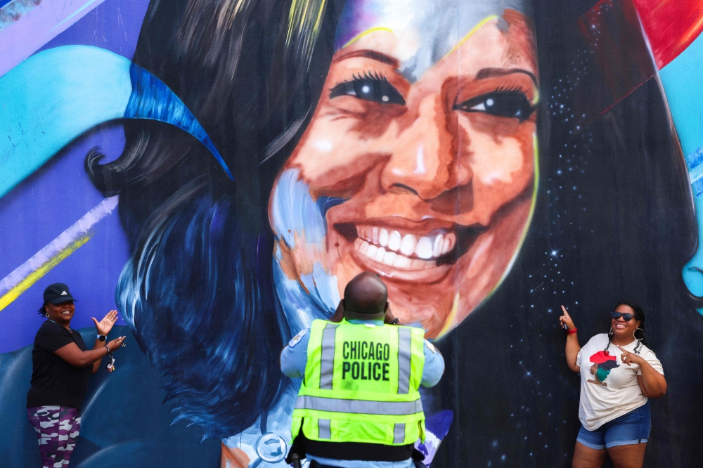 A Chicago police officer takes a picture of people posing before a mural of Democratic presidential nominee US Vice President Kamala Harris outside the United Center ahead of the Democratic National Convention (DNC) in Chicago, Illinois on August 17, 2024. — AFP pic