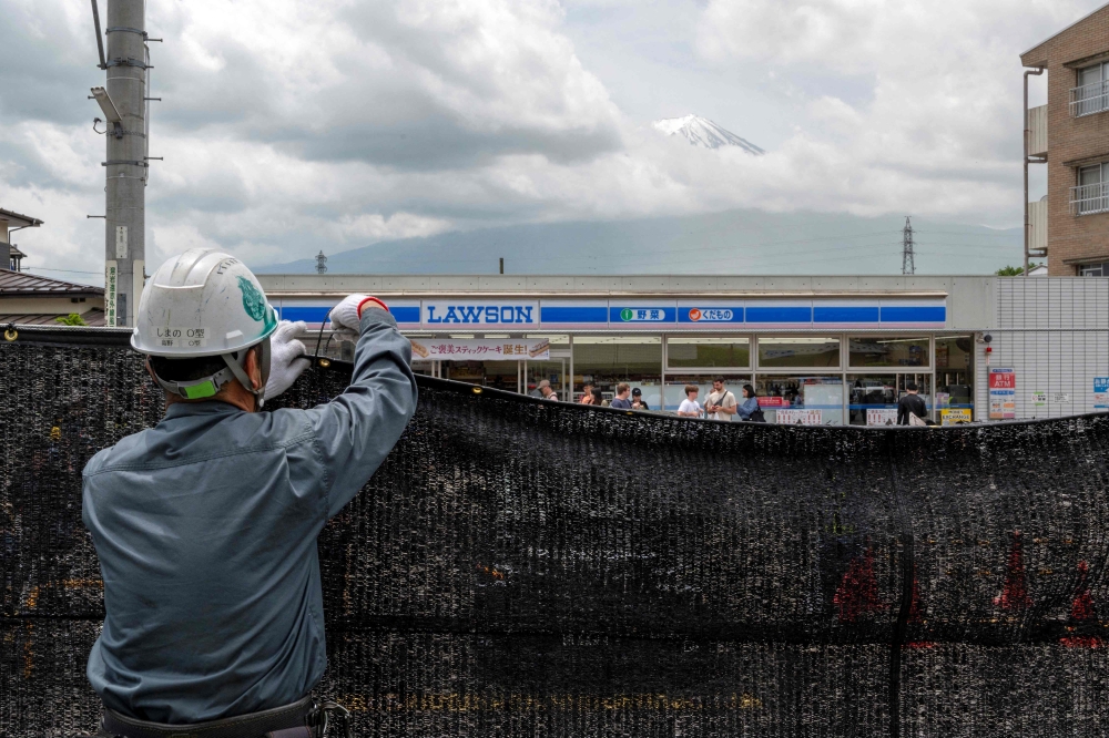This photo taken on May 21, 2024 shows a worker installing a barrier to block the sight of Japan's Mount Fuji emerging from behind a convenience store to deter badly behaved tourists, in the town of Fujikawaguchiko, Yamanashi prefecture. — AFP pic
