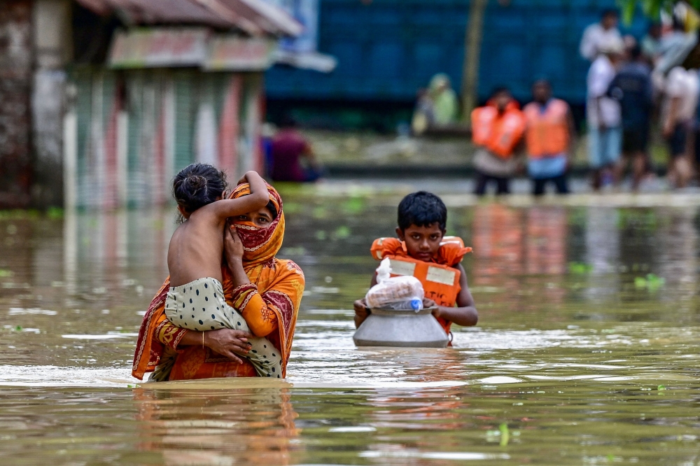 People wade through flood waters after collecting relief materials in Feni, south-eastern Bangladesh. — AFP pic