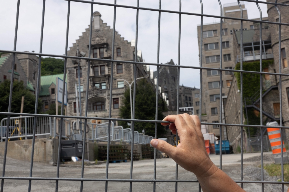 Mohawk Mother Kwetiio looks through a fence at the Royal Victoria Hospital construction site on July 17, 2024, in Montreal. Bulldozers are back at work at Montreal's former Royal Victoria Hospital, but a group of Mohawk mothers have not given up their fight to excavate the site in search of remains of children who went missing some 60 years ago. — AFP pic