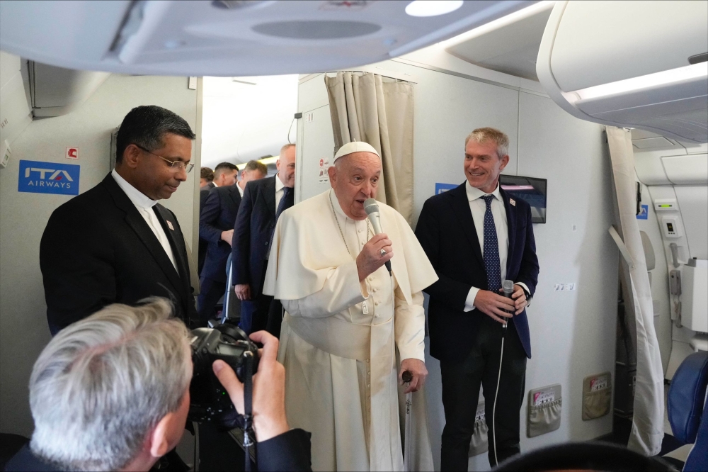 Pope Francis (C), flanked by his spokeperson Maeo Bruni (R), speaks to journalists aboard his flight bound to Jakarta, Indonesia — AFP