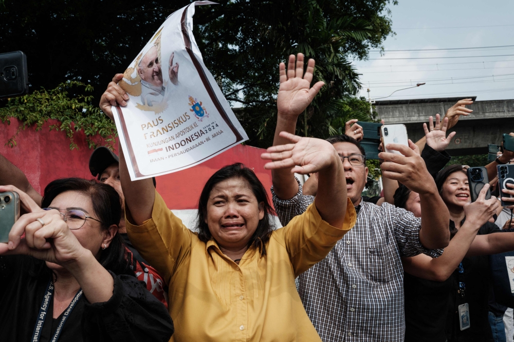 People wave to the vehicle of Pope Francis near the Vatican embassy in Jakarta on September 4, 2024. — AFP pic