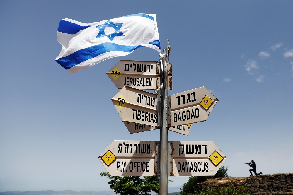 An Israeli flag is seen on top of signs pointing out distances to different cities, on Mount Bental, an observation post in the Israeli-occupied Golan Heights in Israel. — Reuters pic