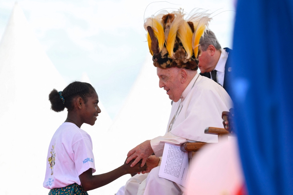 Pope Francis, seen wearing a traditional headdress, interacting with a youth during a meeting with Catholic faithful of the diocese of Vanimo in front of Holy Cross Cathedral in Vanimo, Papua New Guinea, on September 8, 2024. — AFP pic
