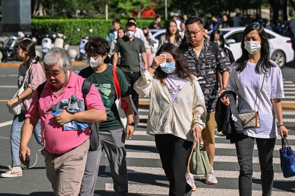 People cross a street amid hot weather conditions in Beijing on August 27, 2024. — AFP pic