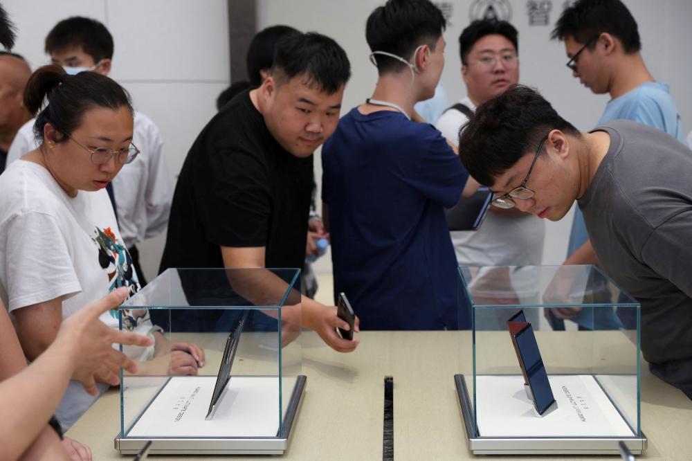 People look at Huawei's Mate XT tri-foldable smartphones displayed in glass cases at a Huawei flagship store in Beijing, China. — Reuters pic
