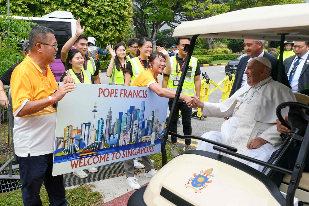 In this handout photograph taken on September 11, 2024 and released by Vatican Media, Pope Francis (2nd right) greets Catholic faithful welcoming him with a banner after his arrival in Singapore. — AFP pic