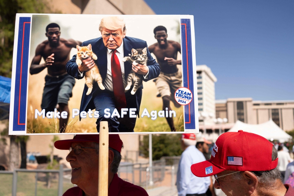 A man carries an AI-generated image of former US President and Republican presidential candidate Donald Trump carrying cats away from Haitian immigrants, a reference to falsehoods spread about Springfield, Ohio, during a campaign rally for Trump at the Tucson Music Hall in Tucson, Arizona, September 12, 2024 — AFP pic