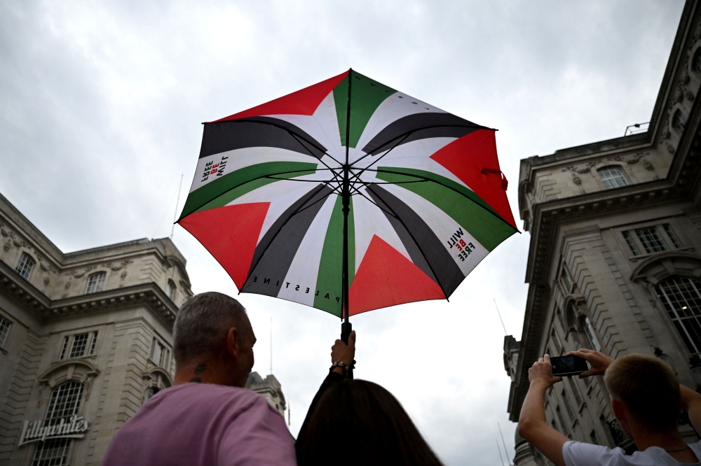 A person holds an umbrella displaying the Palestinian flag during a march through London, during a National Day of Action for Palestine on September 7, 2024. — AFP pic