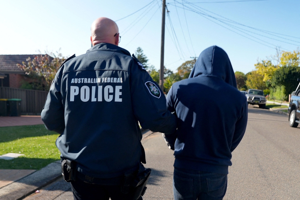 This undated handout photo provided by the Australian Federal Police (AFP) on September 18, 2024, shows an Australian Federal Police officer arresting a suspect allegedly involved in an encrypted messaging app used by criminals worldwide to facilitate drug deals and order killings. — AFP pic