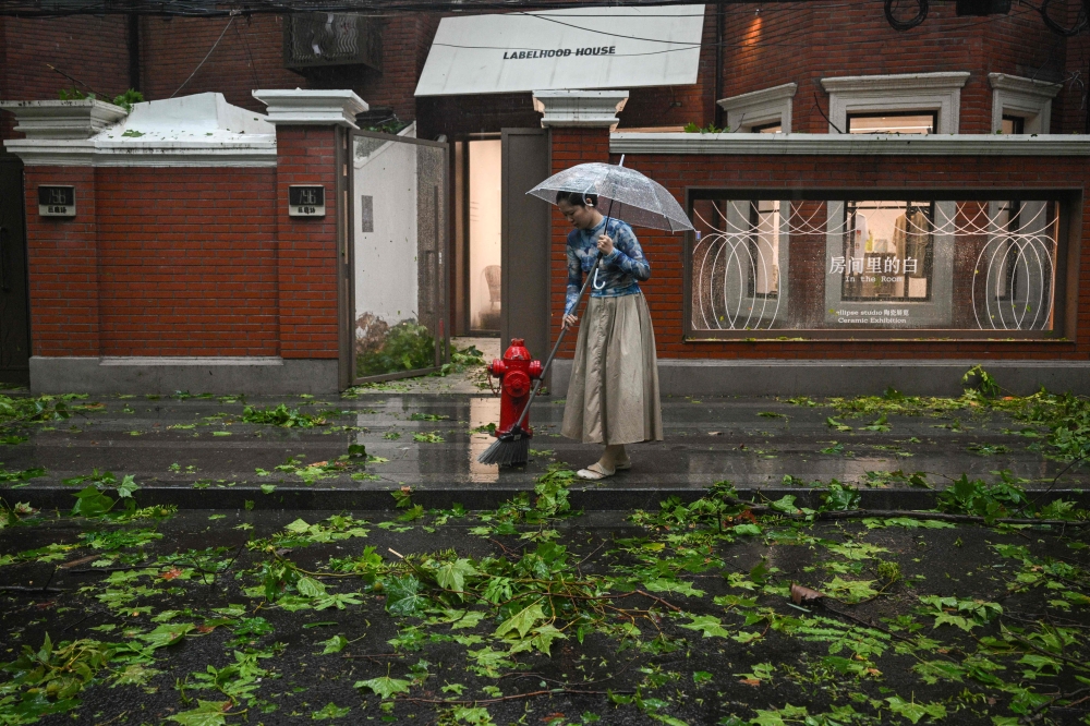 A woman sweeps tree branches and leaves outside a shop brought down during the passage of Typhoon Bebinca in Shanghai on September 16, 2024. — AFP pic