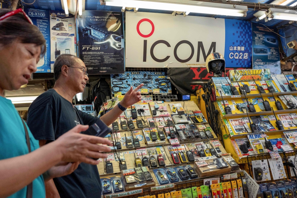 People walk past a sign with the logo of Japanese walkie-talkie maker Icom at a shop that specialises in wireless devices in Tokyo's Akihabara electric district on September 19, 2024. — AFP pic