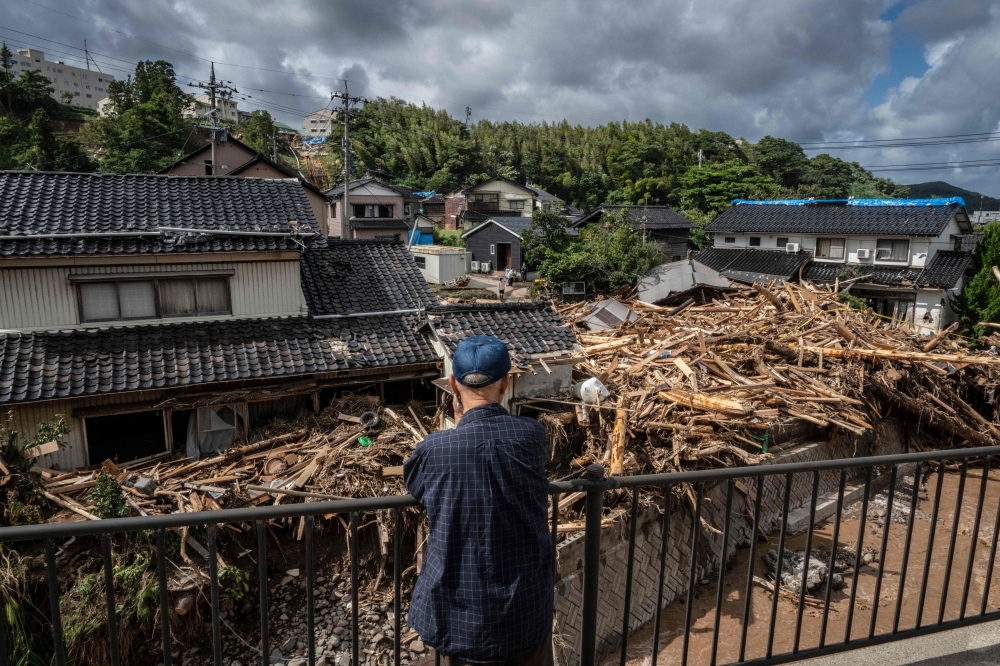 A man looks on as debris washed away from flooding is seen piled by houses along the Tsukada river following heavy rain in Wajima city, Ishikawa prefecture on September 23, 2024. Heavy rain that triggered floods and landslides on a Japanese penisula recovering from an earthquake this year killed at least six people, local media reported on September 23. — AFP pic