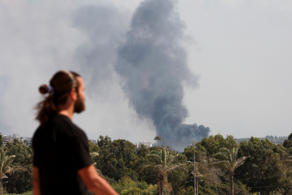 A man watches as smoke billows over southern Lebanon following Israeli strikes, amid ongoing cross-border hostilities between Hezbollah and Israeli forces, as seen from Tyre, southern Lebanon September 23, 2024. — Reuters pic