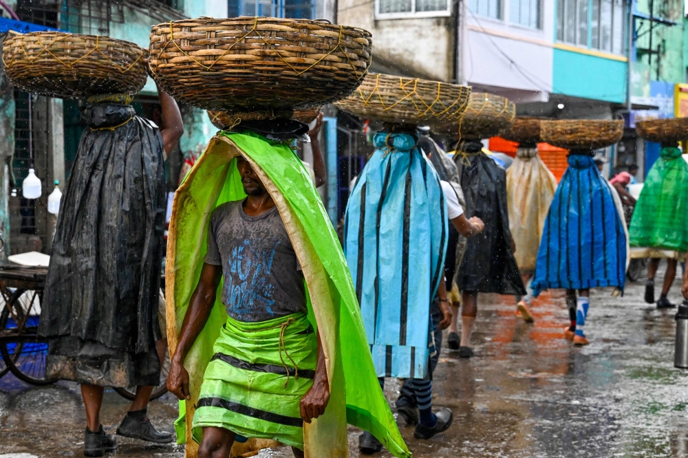  In this photo taken on September 10, 2024, labourers carrying Hilsa fish in bamboo baskets, wear plastic sheets as it rains at a wholesale market in Diamond Harbour, in the Indian state of West Bengal. — AFP pic