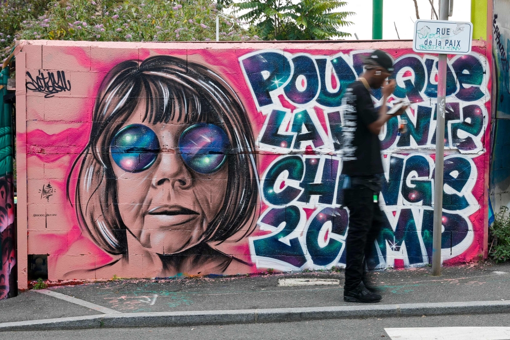 A man walks past a mural created by Maca_dessine depicting Gisele Pelicot in Gentilly, south of Paris on September 21, 2024 as her former partner Dominique Pelicot is accused of drugging her for nearly ten years and inviting strangers to rape her at their home in Mazan. — AFP pic