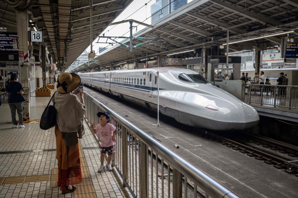 A woman takes photographs of her child in front of a Shinkansen at Tokyo Station in Tokyo July 25, 2024. — AFP pic