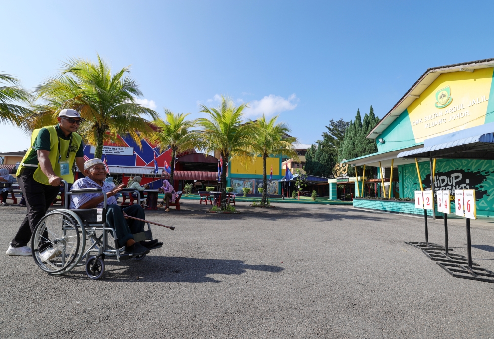 An election officer assisting a senior citizen in a wheelchair to get to his voting stream at the SMK Sultan Abdul Jalil in Kluang, Johor for the Mahkota by-election on September 28, 2024. — Bernama pic