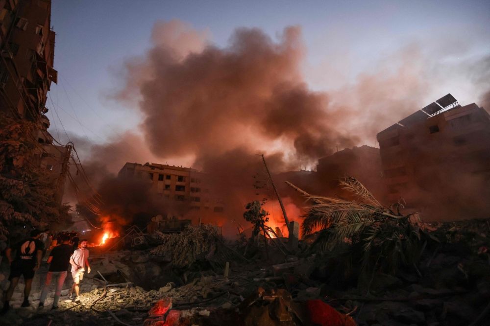 Smoke rises from the smouldering rubble as people gather at the scene of Israeli air strikes said to have flattened some buildings in the Haret Hreik neighbourhood of Beirut’s southern suburbs on September 27, 2024. — AFP pic