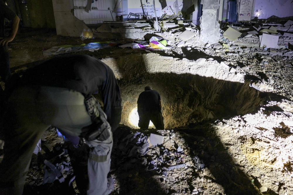 Members of Israel's Home Front Command and police forces inspect a crater left by an exploded projectile at a heavily-damaged school building in Israel's southern city of Gedera on October 1, 2024, after Iran launched a barrage of missiles at Israel. — AFP pic