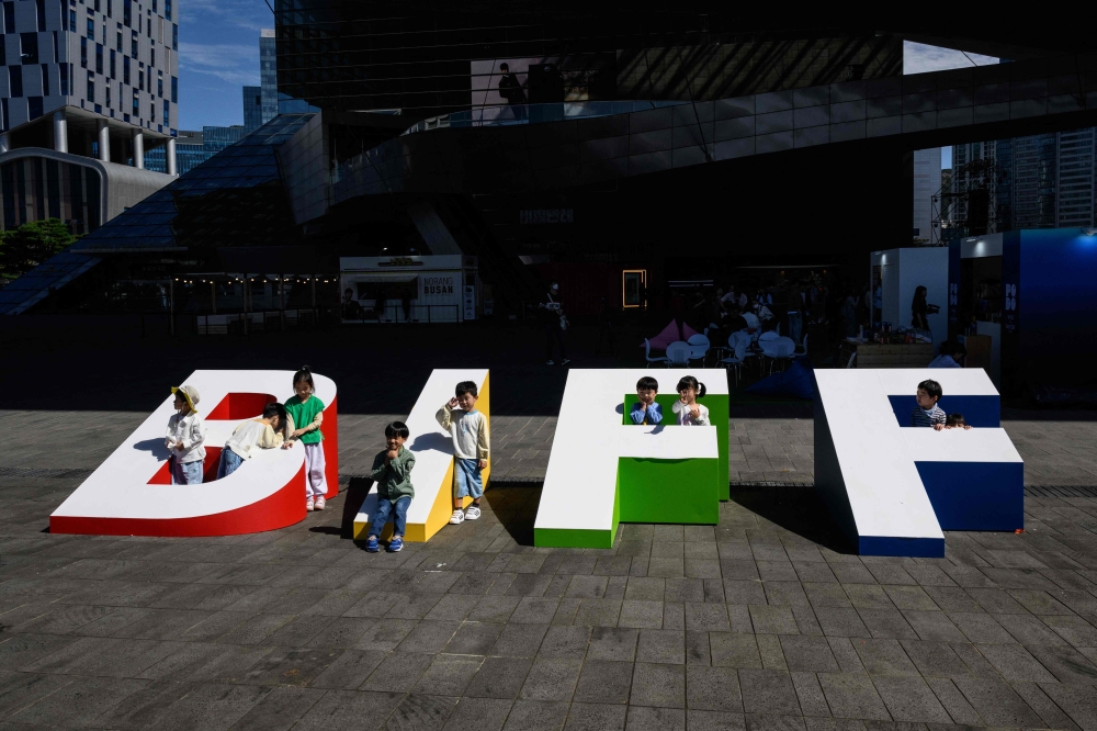 In this file photo taken on October 4, 2023, children pose for photos next to large letters displayed for the 28th Busan International Film Festival (BIFF) at the Busan Cinema Centre in Busan. A Netflix period war drama produced by South Korean filmmaker Park Chan-wook will open Asia's largest film festival today, the first time a streaming title has kicked off the event. — AFP pic