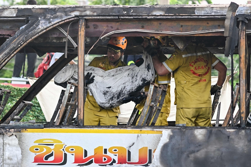 A rescue worker carries the wrapped-up body of a victim following a fire on a bus that was carrying students and teachers on the outskirts of Bangkok on October 1, 2024. — AFP pic