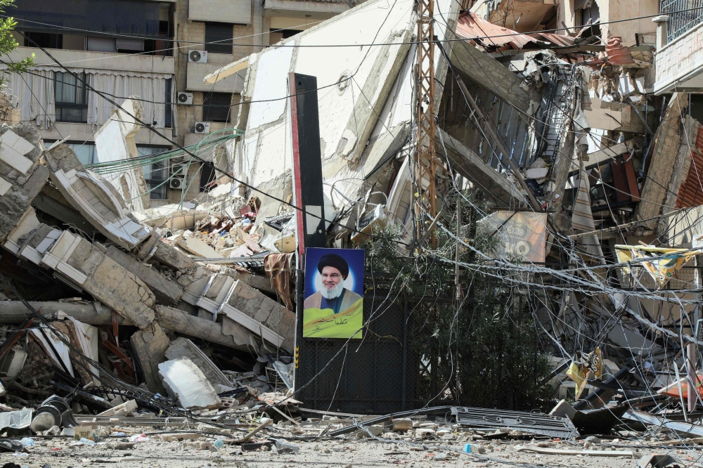A picture taken during a tour organised by Hezbollah media office on October 2, 2024 shows a portrait of the group’s slain leader Hassan Nasrallah hanging on the rubble of a building destroyed in an Israeli airstrike on a neighbourhood in Beirut’s southern suburbs. — AFP pic