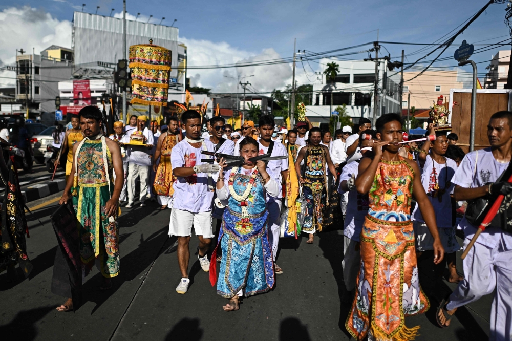 Sirinnicha Thampradit, a devotee of the Jor Soo Gong Naka shrine, walks with swords pierced through her cheek as she takes part in a procession during the annual vegetarian festival in Phuket on October 4, 2024. — AFP pic 