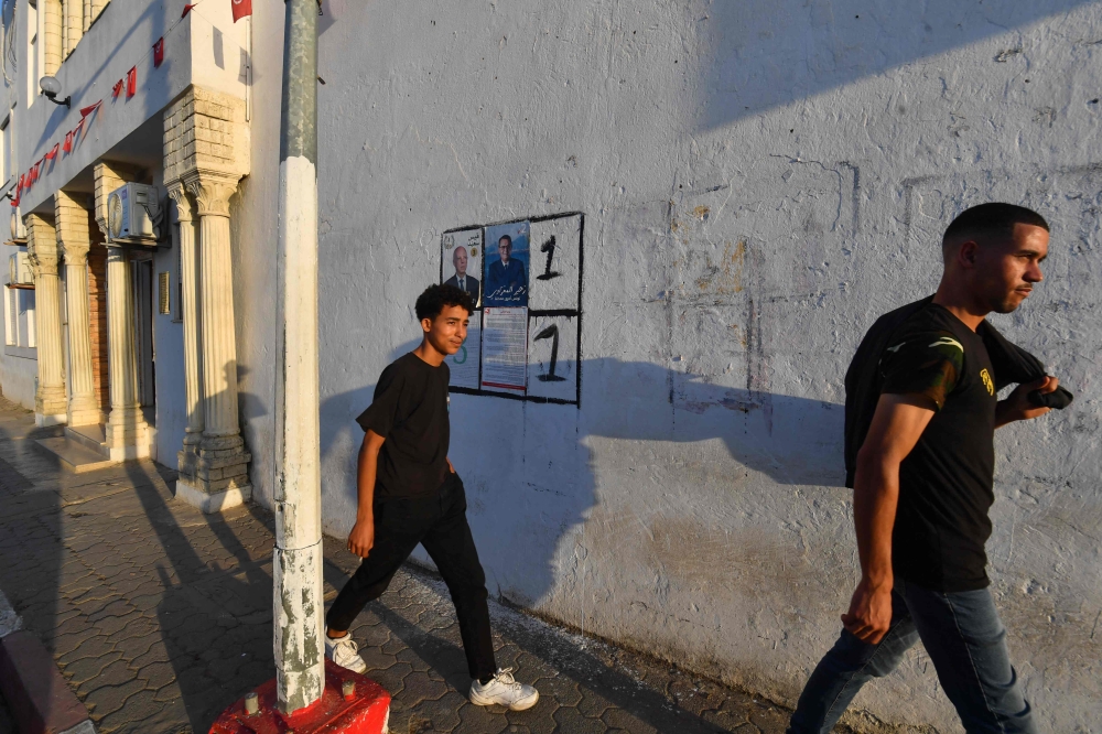 Young men walk past portraits of the two presidential candidates on a wall in north-western Tunisia's Fernana town on September 25, 2024. — AFP pic