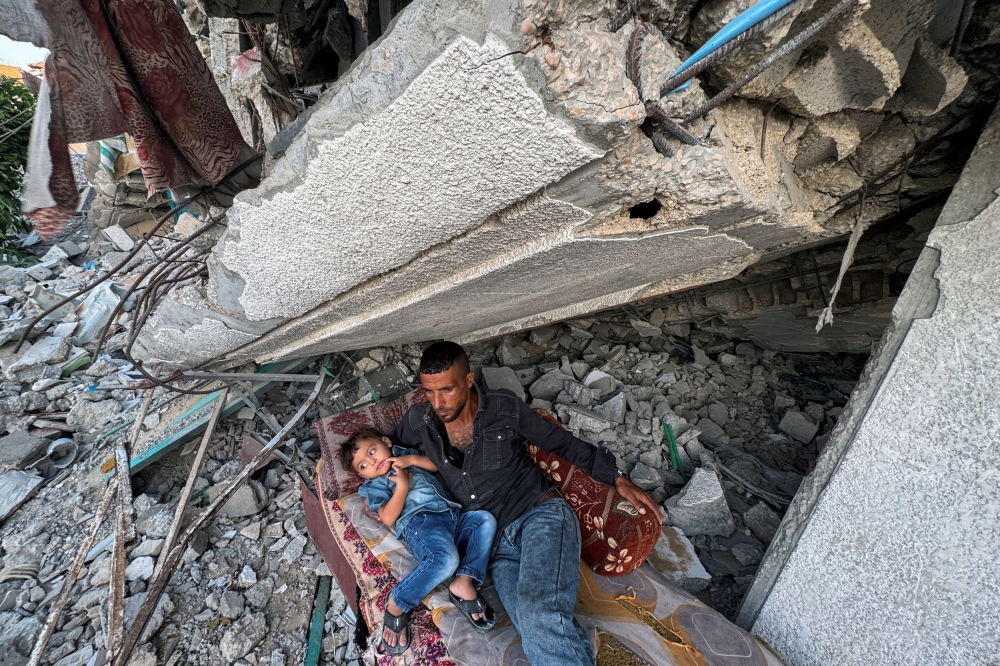 A Palestinian man rests with his son under the rubble of their destroyed house, amid the ongoing conflict between Israel and Hamas, in Khan Younis in the southern Gaza Strip September 26, 2024. — Reuters pic