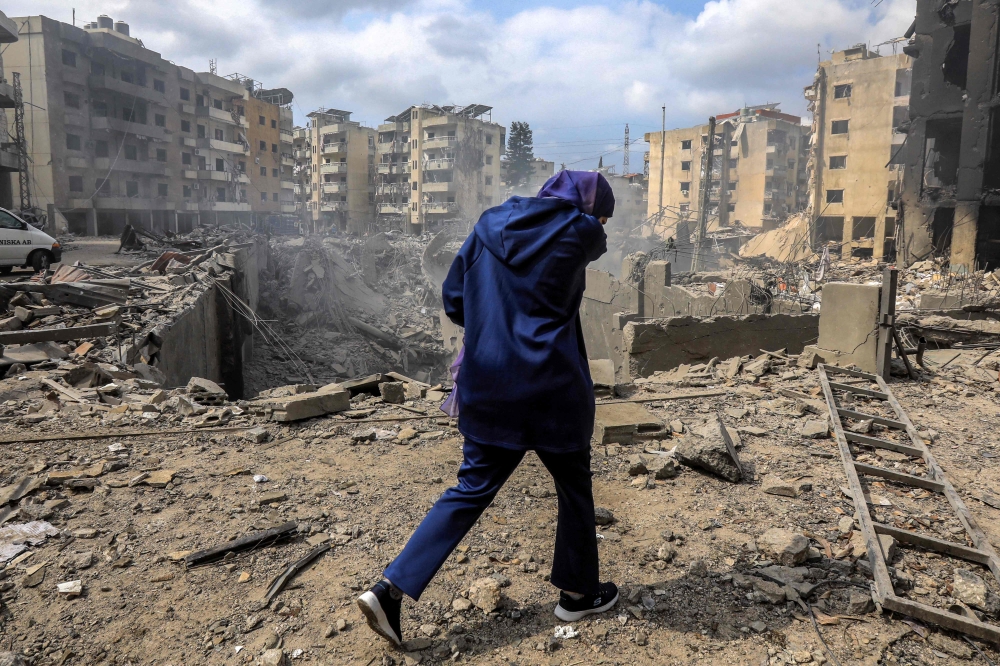 A woman walks past a crater where a collapsed building stood following an overnight Israeli air strike on the neighbourhood of Kafaat in Beirut's southern suburbs, on October 7, 2024. — AFP pic