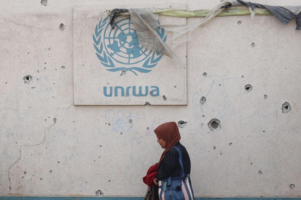 A Palestinian woman walks past a damaged wall bearing the UNRWA logo at a camp for internally displaced people in Rafah in the southern Gaza Strip on May 28, 2024, amid the ongoing conflict between Israel and the Palestinian Hamas militant group. — AFP pic