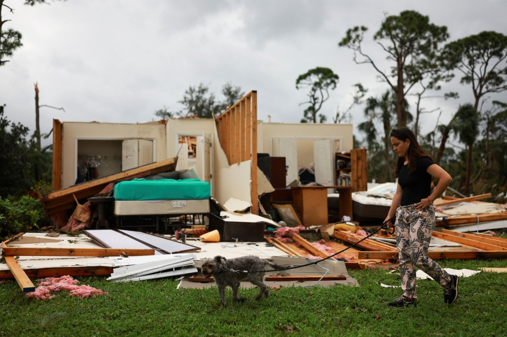 A woman walks a dog next to a damaged house following Hurricane Milton landfall, in Lakewood Park, near Fort Pierce, in St. Lucie County, Florida October 11, 2024. — Reuters pic