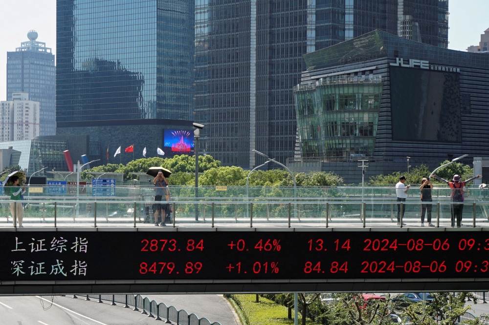 People take pictures on an overpass with a display of stock information in front of buildings in the Lujiazui financial district in Shanghai. — Reuters pic
