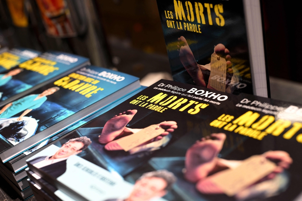 This photograph taken on October 10, 2024 shows books by Belgian forensic doctor Philippe Boxho during a conference about his work in Blegny. Boxho recounts his autopsies with a scathing humour in books that fascinate the public and also allow him to popularise a little-known profession. — AFP pic