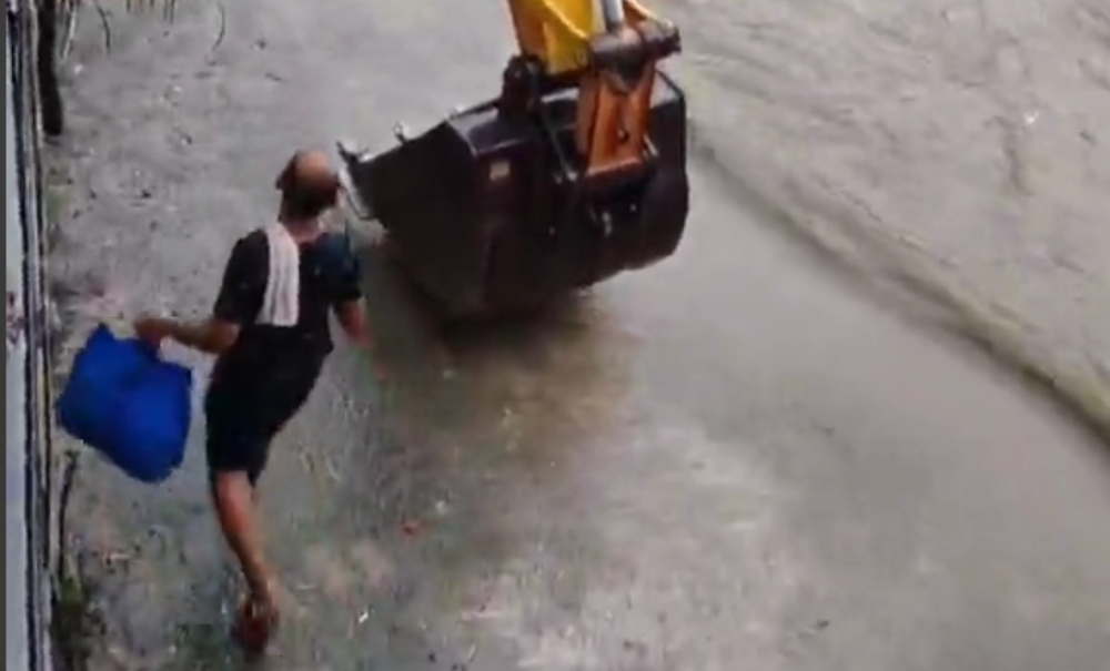 A screen capture from a video shows a man climbing into the bucket of an excavator.