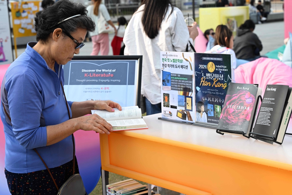 A woman reads a book by South Korean author Han Kang, who won the 2024 Nobel Prize in Literature, displayed during an outdoor library event at Gwanghwamun square in central Seoul on October 11, 2024. — AFP pic