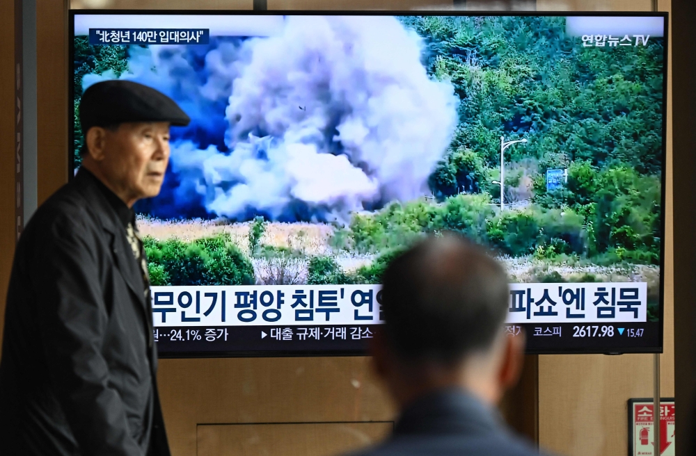 A man walks past a television screen showing a news broadcast with footage of an explosion on a road connecting North and South Korea on October 15, 2024, at a train station in Seoul on October 16, 2024.  — AFP pic
