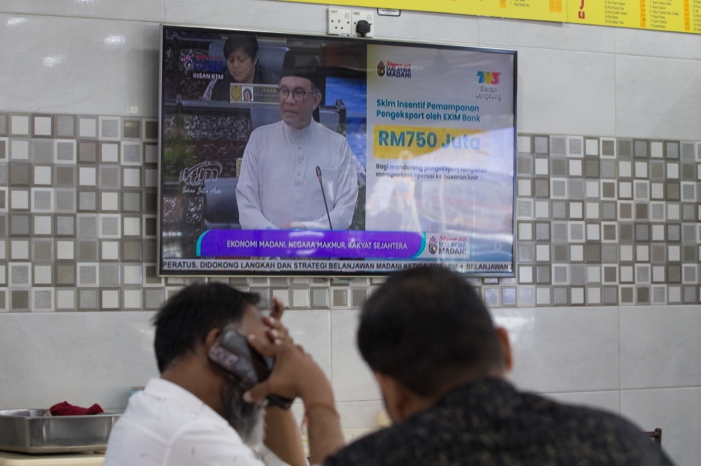 People at a restaurant watch Prime Minister Anwar Ibrahim deliver the 2025 national budget on television yesterday. — Devan Manuel