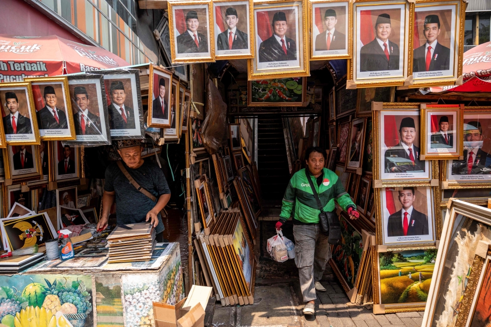 A taxi moto driver walks past pictures of Indonesia's president-elect Prabowo Subianto and vice president-elect Gibran Rakabuming Raka ahead of their inauguration today. — AFP pic 