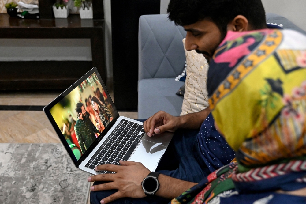 In this photograph taken on August 31, 2024, Ezza Nawaz (right), a textile designer who got married through Muzz app, sits next to her husband Waseem Akhtar while watching their wedding photographs on a laptop at their residence, in Lahore. — AFP pic 