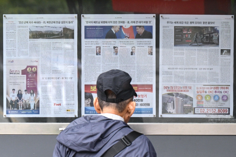 A man walks past a newspaper displayed on a street for the public in Seoul on October 21, 2024, with coverage on North Korea’s decision to deploy thousands of soldiers to Ukraine’s front lines and a photo (centre) of North Korean leader Kim Jong Un and Russia’s President Vladimir Putin toasting at a banquet in Pyongyang earlier this year. — AFP pic 