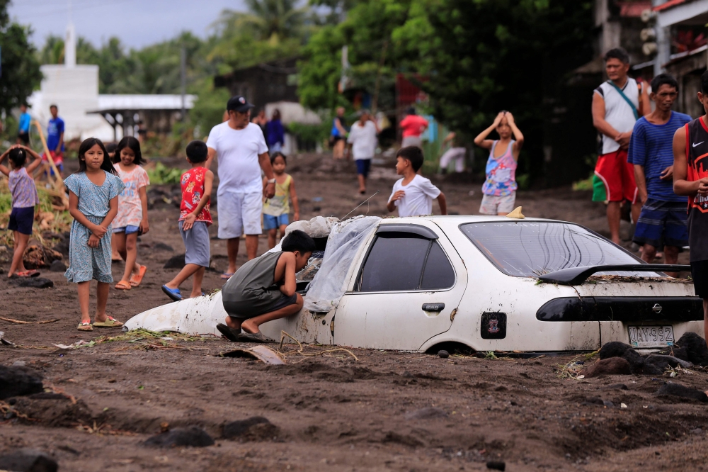 Residents look at a car buried by volcanic ash which cascaded into a village triggered by heavy rains brought about by Tropical Storm Trami at a village in Guinobatan town, Albay province South of Manila on October 23, 2024. — AFP pic