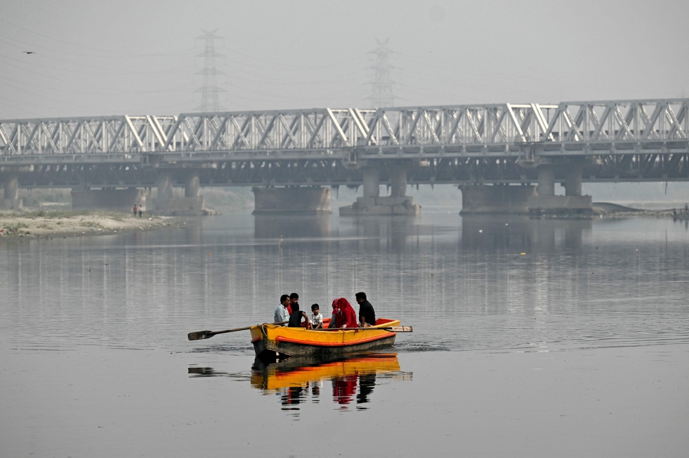 People take a boat ride in the polluted waters of river Yamuna in New Delhi on October 21, 2024. — AFP pic