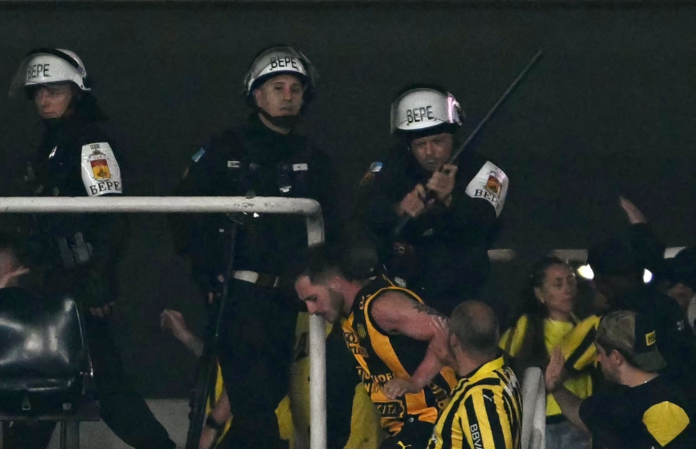 A police officer beats a fan of Penarol at the end of the Copa Libertadores semi-final first leg football match between Brazil’s Botafogo and Uruguay’s Pe’arol at the Olimpico Nilton Santos stadium in Rio de Janeiro, Brazil, on October 23, 2024. — AFP pic