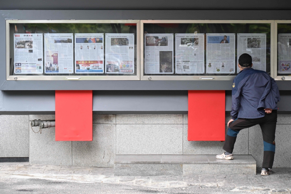 A man reads a newspaper displayed on a street for the public in Seoul on October 21, 2024, with coverage on North Korea's decision to deploy thousands of soldiers to Ukraine's front lines. — AFP pic